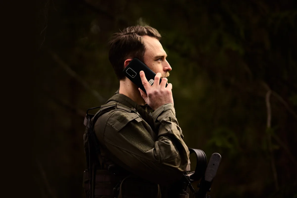 Soldier in field gear using a secure mobile phone in a forest, illustrating secure communications for national security